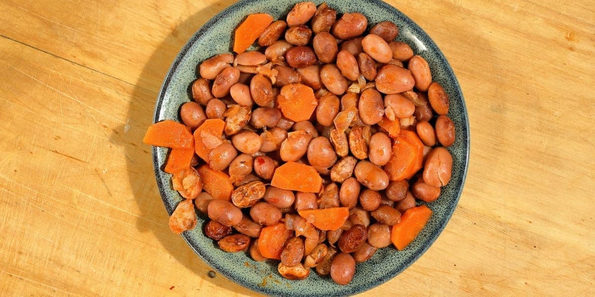A plate of cooked beans and sliced carrots on a wooden table