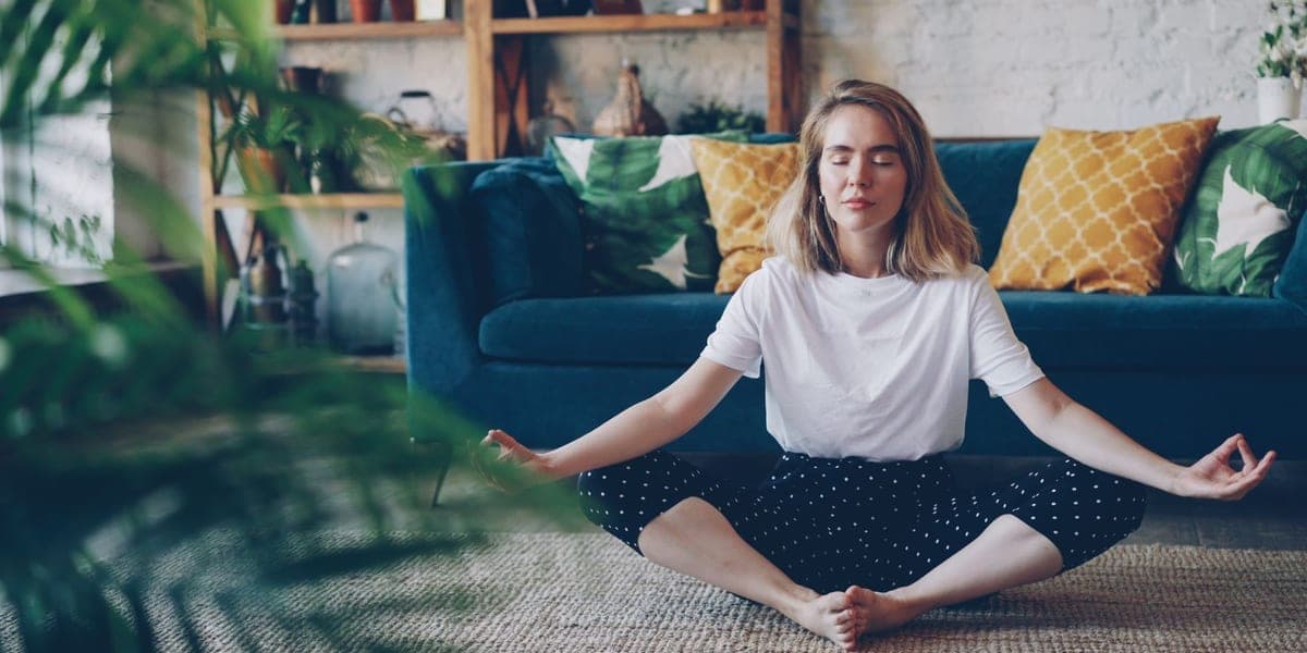 Woman sitting cross-legged with eyes closed in front of a blue sofa.
