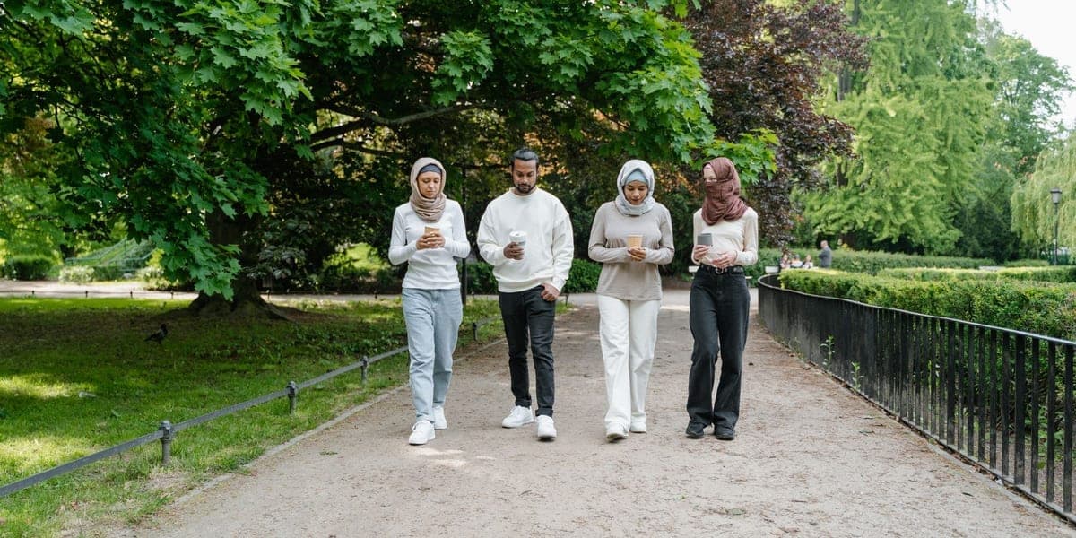 Four adults walking along a tree-lined park path.