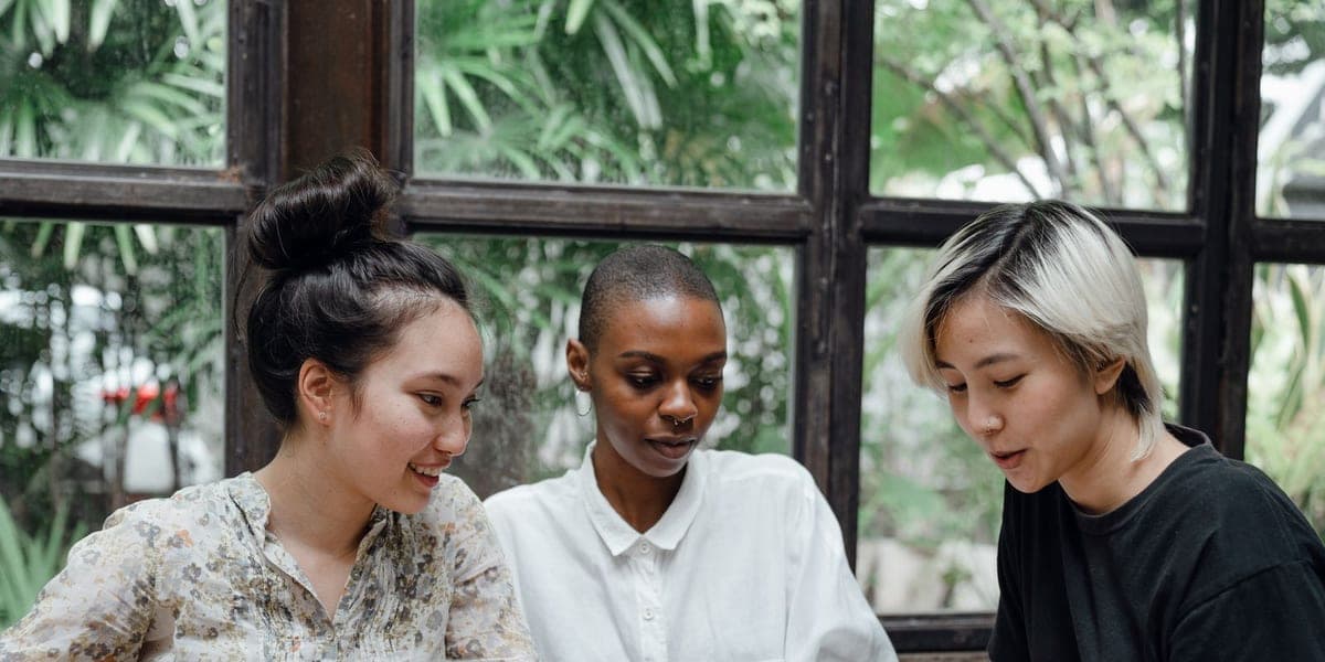Three women at a cafe table with a cup of coffee, laptop and phone.