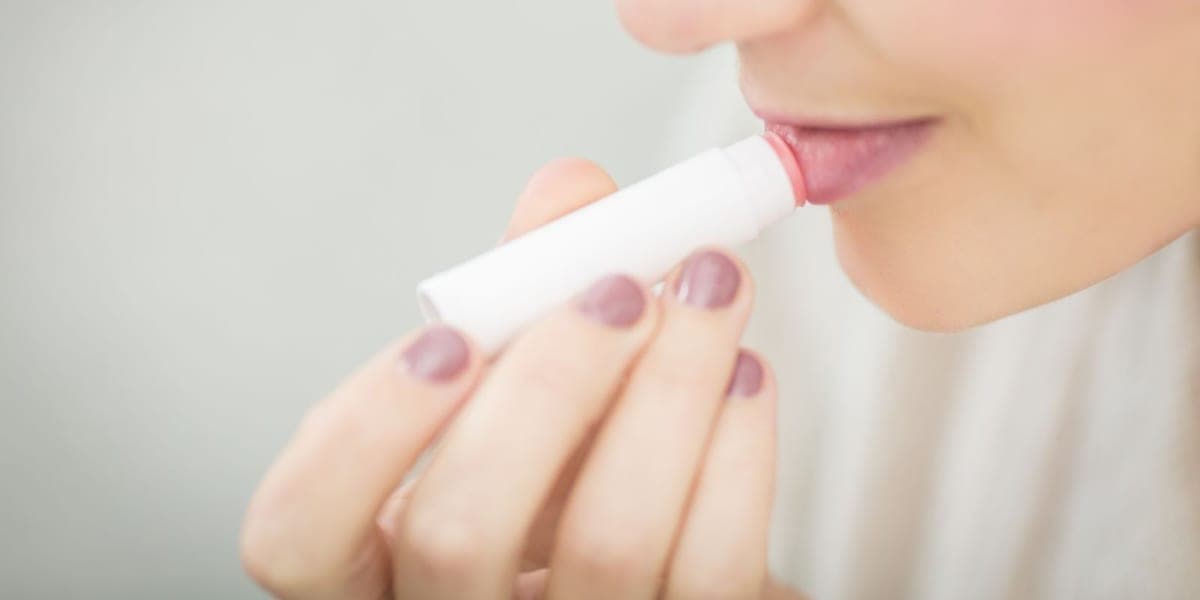 Close-up of a person applying lip balm from a white tube
