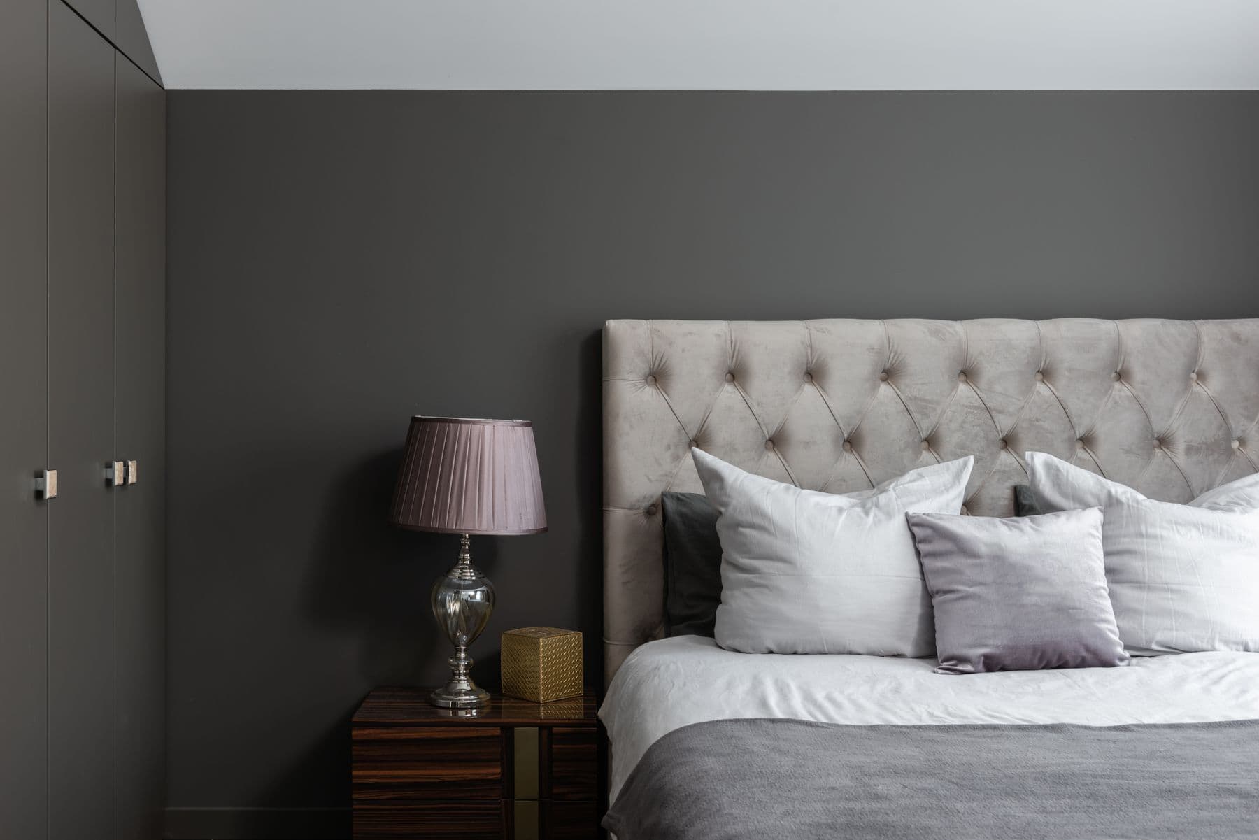 Bed with soft gray and white pillows beside a lamp and bedside table.