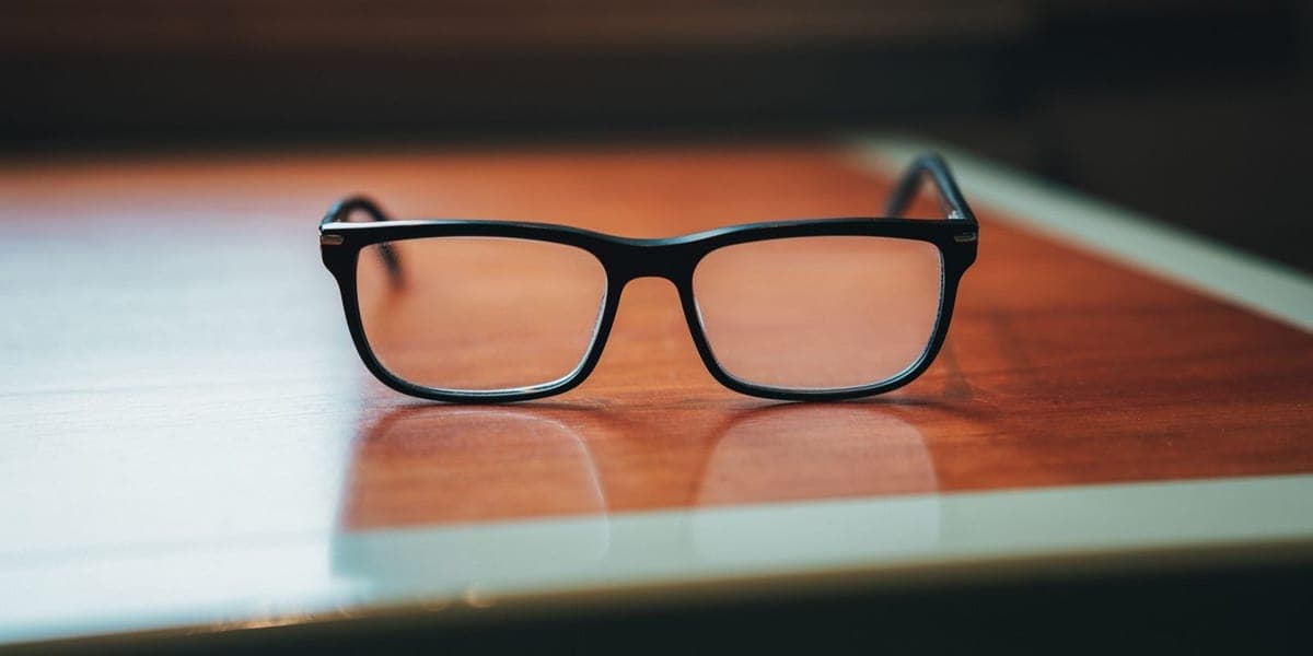 Black rectangular eyeglasses resting on a polished wooden table.