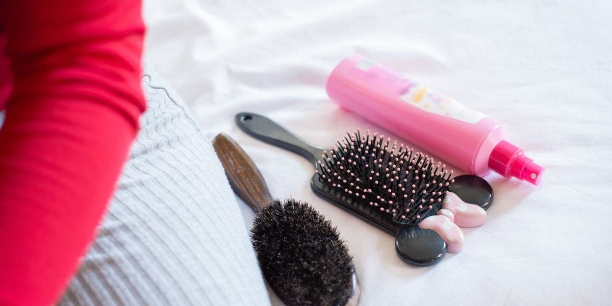 Hair brushes and a pink spray bottle arranged on white fabric.