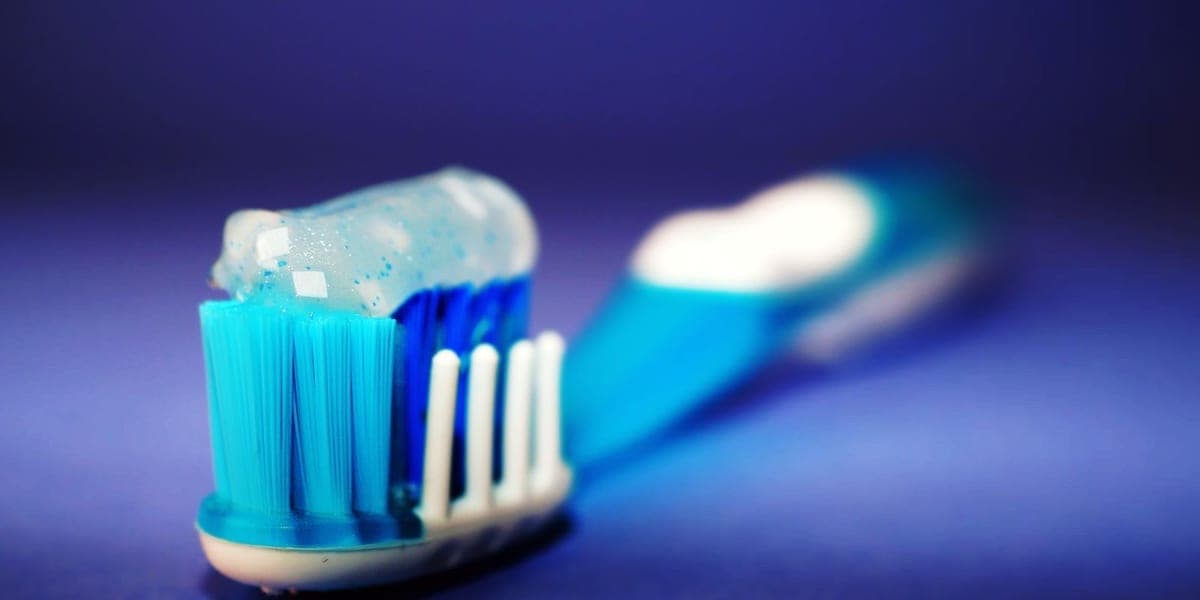 A close-up of blue toothpaste on a toothbrush against a blue background.