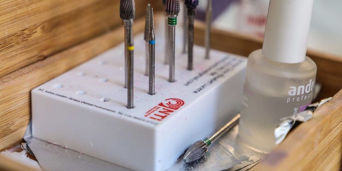 Metal manicure drill attachments and a nail product bottle inside a wooden box.