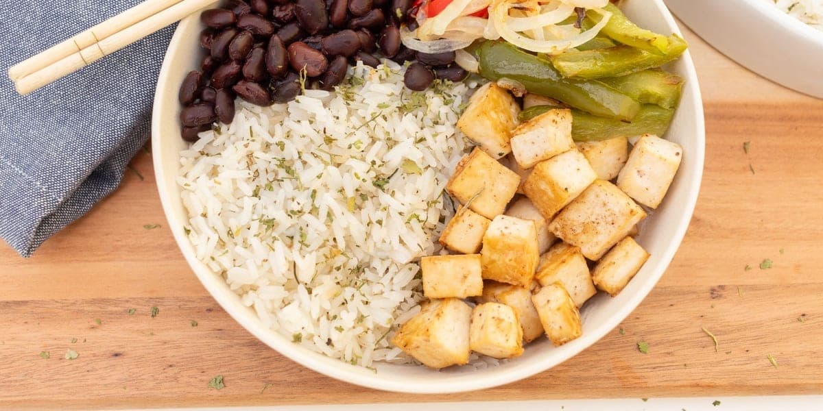Bowl of rice with tofu cubes, black beans, peppers, and onions.