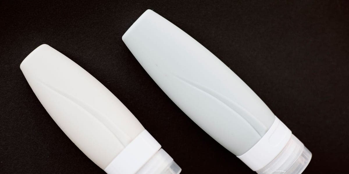 Two pale cosmetic containers with clear caps on a dark background