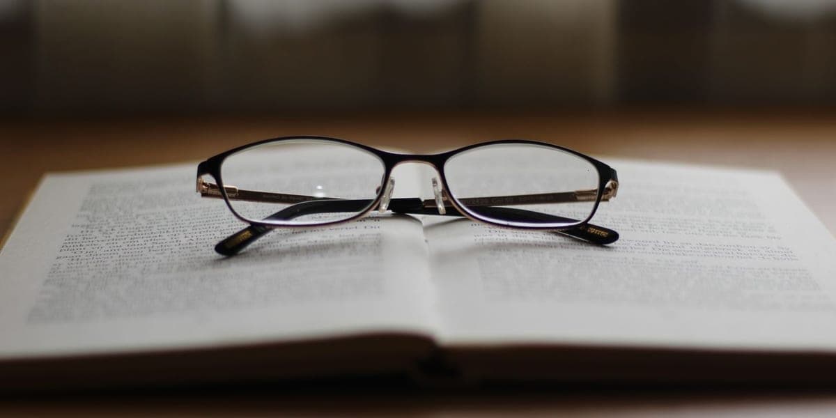 Dark-framed eyeglasses resting across the pages of an open book.