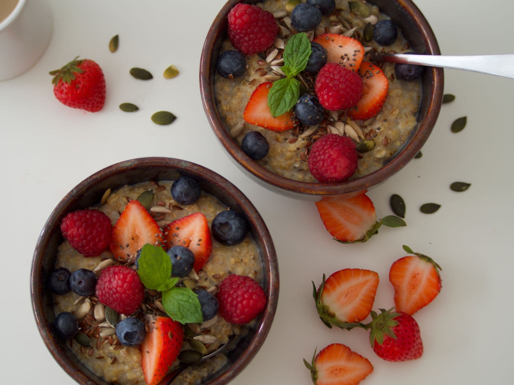 Two bowls of oatmeal topped with strawberries, raspberries, blueberries, and seeds.