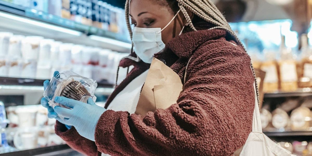 A shopper wearing a mask examines a packaged food container in a supermarket