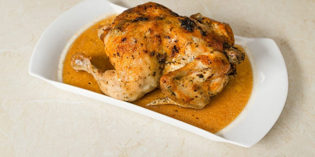 A whole roasted chicken with gravy on a white platter