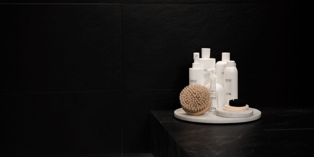 White cosmetic bottles and brushes on a round tray against a dark background
