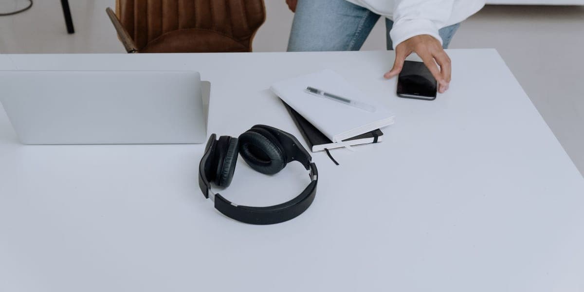 Black over-ear headphones beside a laptop and notebooks on a white desk
