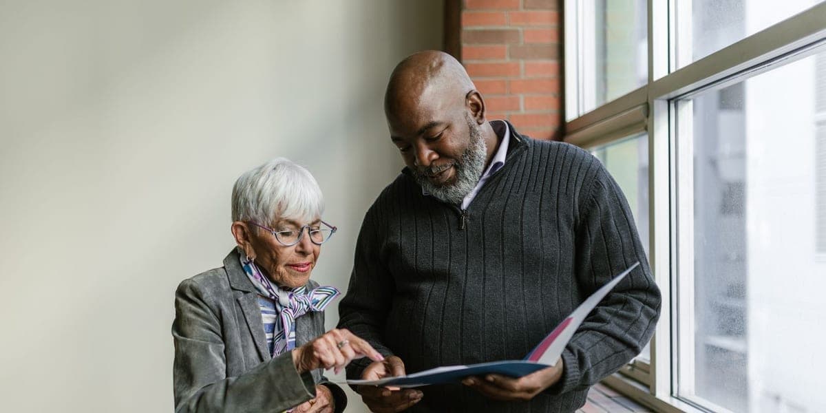 Two older adults reviewing an open folder together beside a window.