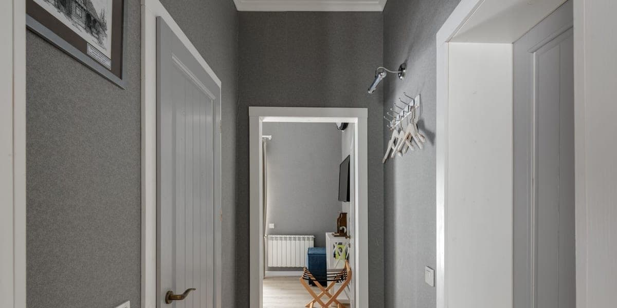 A hallway with gray walls, light wooden flooring and open doorways.