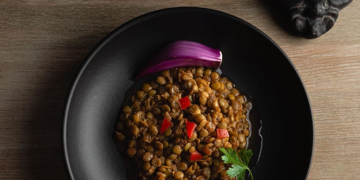 Cooked lentils with red pepper, red onion and parsley in a black bowl.