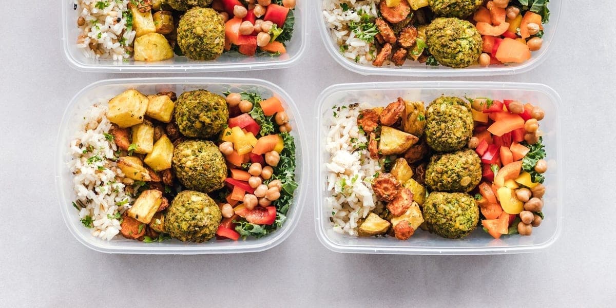 Four food containers holding rice, vegetables, chickpeas and falafel.