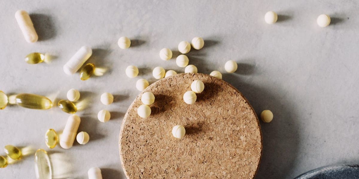 Tablets and capsules arranged beside a round cork lid on a pale surface.