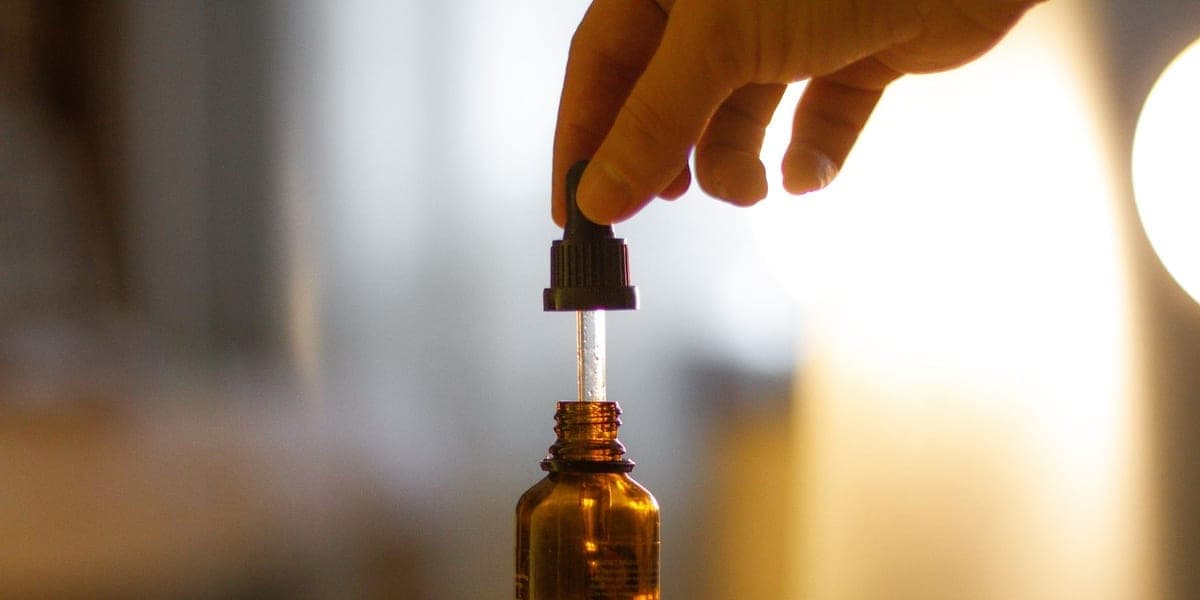 Hand lifting a glass dropper from an amber bottle on a table.