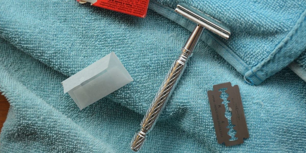 A silver safety razor, blade and packaging arranged on a blue towel