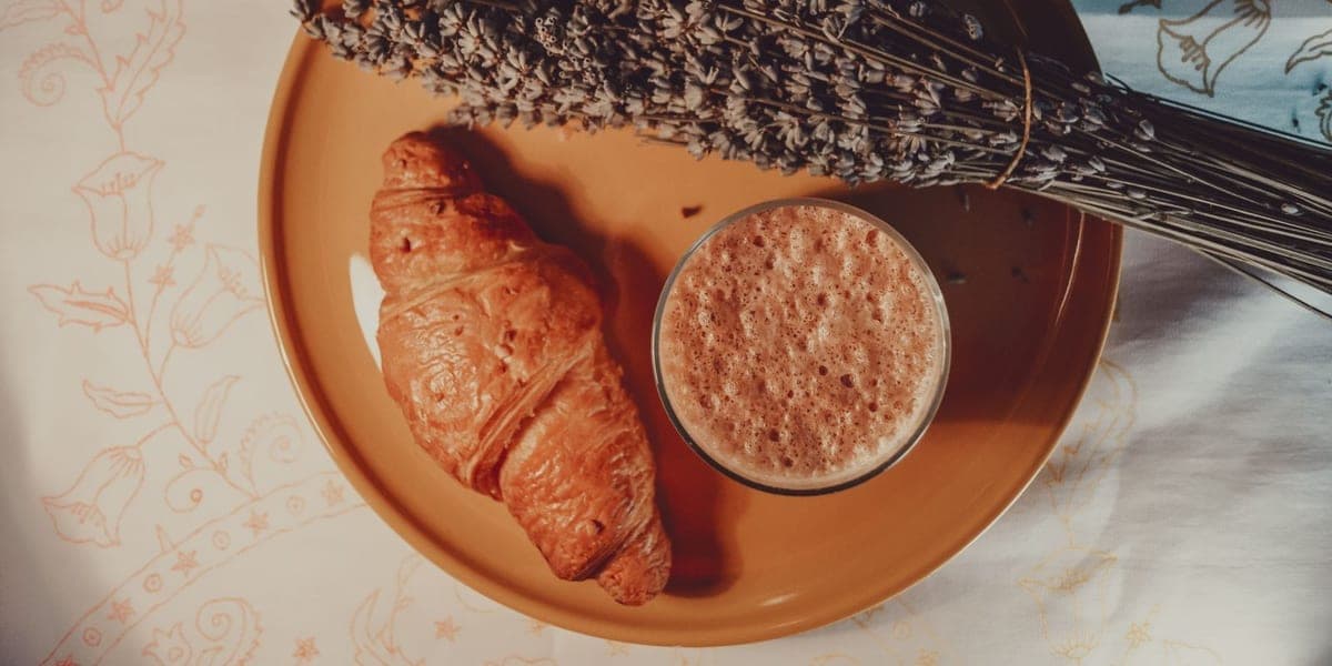 Overhead view of coffee, a croissant and a bundle of dried lavender on a plate