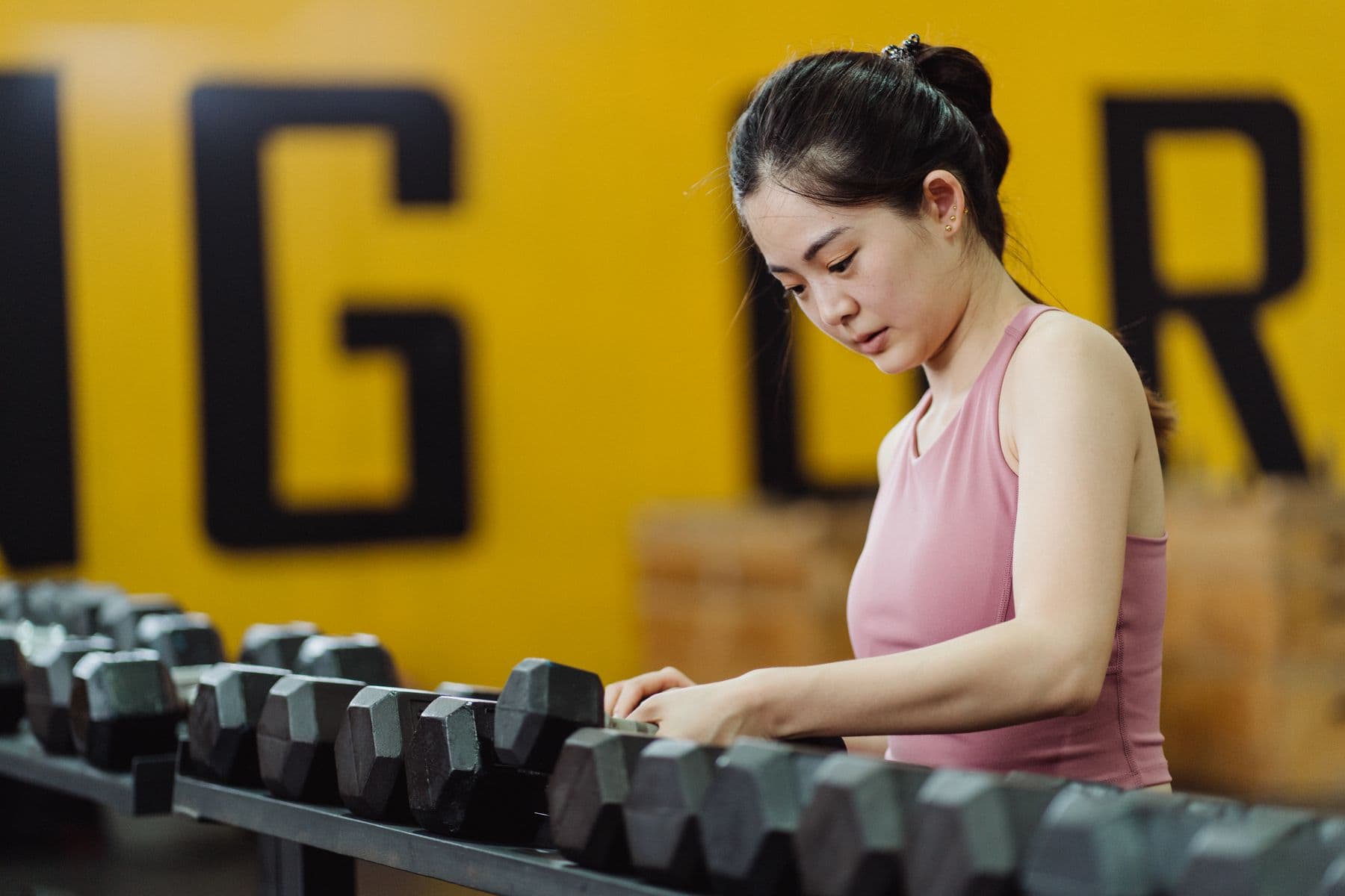Woman in a pink exercise top selecting dumbbells from a gym rack.
