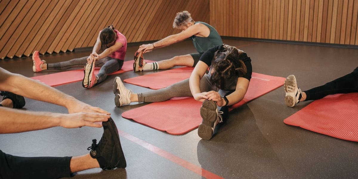 Adults doing seated stretches on pink exercise mats in a studio.