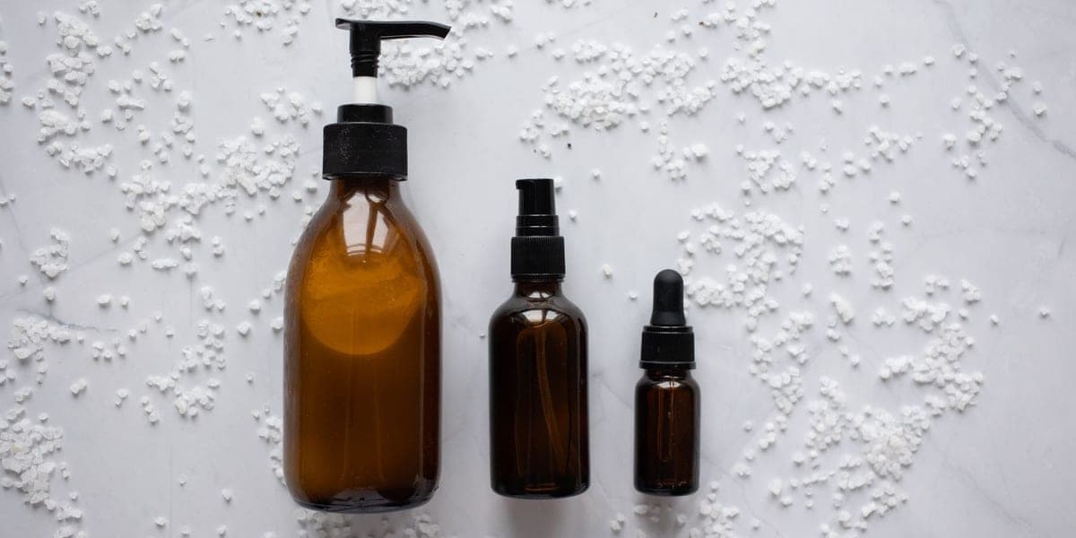 Three amber cosmetic bottles arranged on a pale marble surface