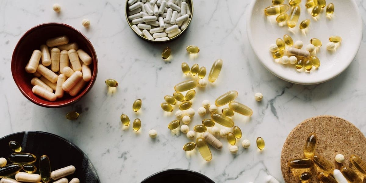 Assorted capsules and tablets arranged in small bowls on a pale marble surface