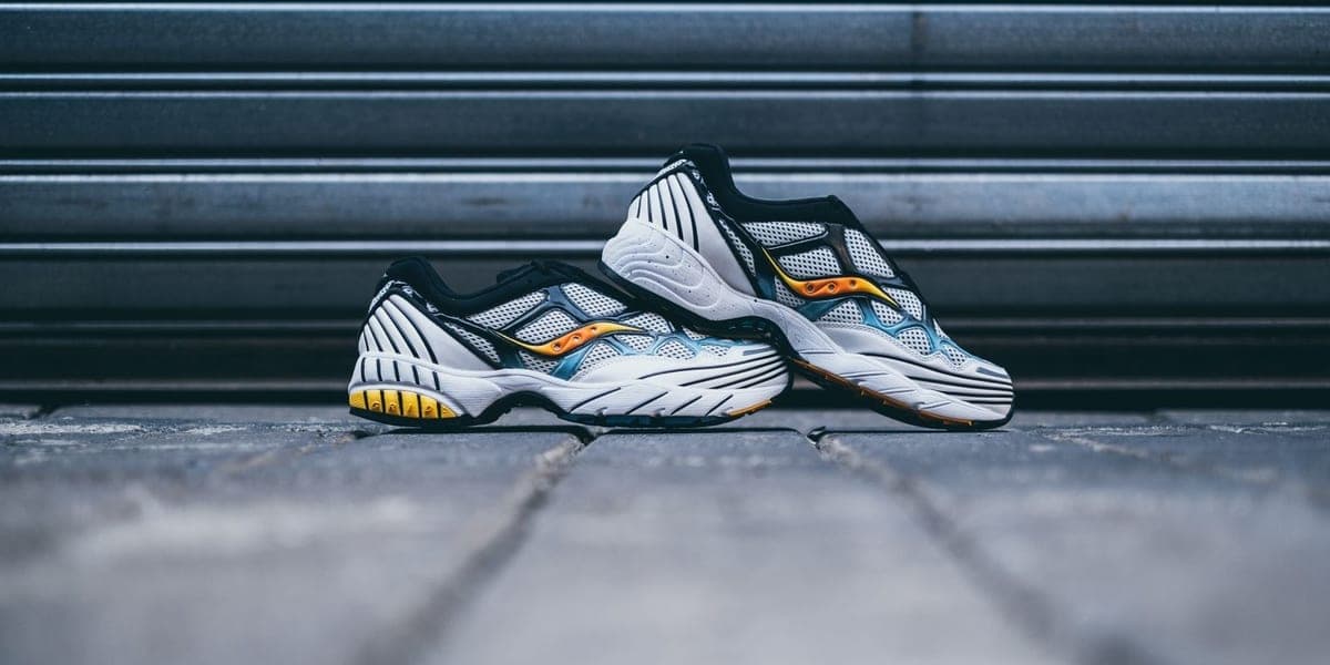 A pair of gray athletic shoes with yellow accents on pavement