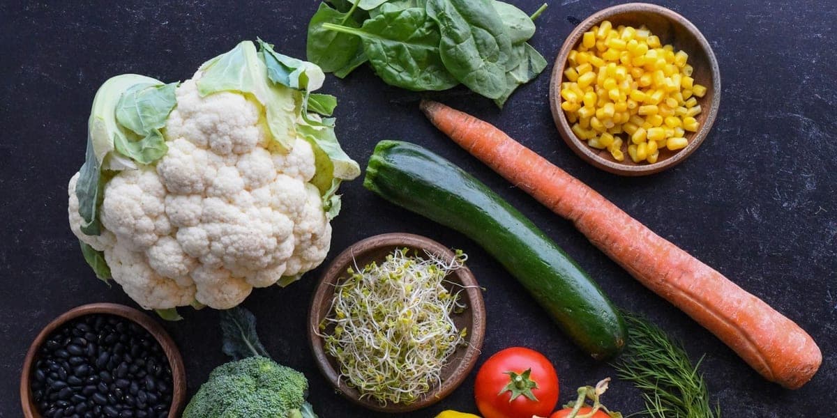 An assortment of vegetables, herbs and a lemon arranged on a dark surface
