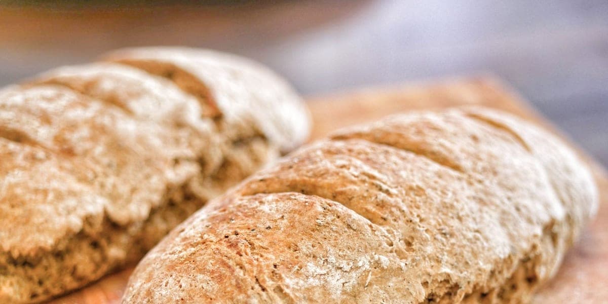 Two flour-dusted bread loaves on a wooden chopping board.